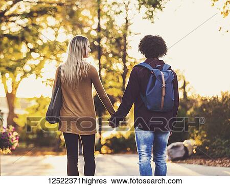 Boyfriend and girlfriend walking away from the camera and holding hands on the university campus at sunset; Edmonton, Alberta, Canada View Large Photo Image Stock Photograph - Boyfriend and girlfriend walking away from the camera and holding hands on the university campus at sunset; Edmonton, Alberta, Canada. Fotosearch