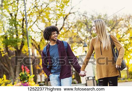 Stock Photograph - Boyfriend and girlfriend walking, talking and holding hands on the university campus at sunset; Edmonton, Alberta, Canada. Fotosearch