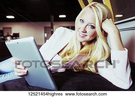 Stock Photograph - Business portrait of a beautiful young millennial businesswoman with long blond hair holding a tablet and posing for the camera in the workplace; Sherwood Park, Alberta, Canada. Fotosearch