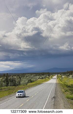 Car driving on the Alaska Highway with stormy clouds overhead, west of Whitehorse, Yukon Territory, Canada, Summer View Large Photo Image Stock Photo - Car driving on the Alaska Highway with stormy clouds overhead, west of Whitehorse, Yukon Territory, Canada, Summer . Fotosearch