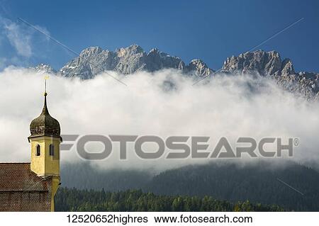 Church spire in the valley with mountain peaks peering out from the clouds covering the mountainside; San Candido, Bolzano, Italy View Large Photo Image Stock Photograph - Church spire in the valley with mountain peaks peering out from the clouds covering the mountainside; San Candido, Bolzano, Italy. Fotosearch