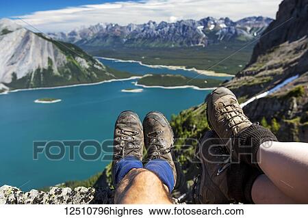 Close-up of a couple's hiking boots over a cliff overlooking a colourful alpine lake and mountain range in the distance; Kananaskis Country, Alberta, Canada View Large Photo Image Stock Photograph - Close-up of a couple's hiking boots over a cliff overlooking a colourful alpine lake and mountain range in the distance; Kananaskis Country, Alberta, Canada. Fotosearch