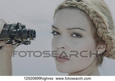 Stock Photograph - Close-up of a young woman looking at the camera and holding binoculars out from her face; Alicante, Spain. Fotosearch