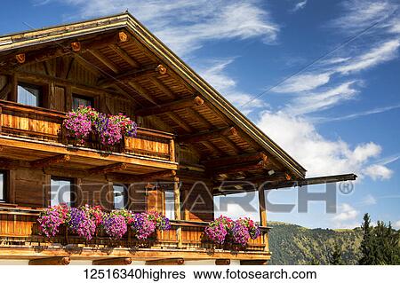 Stock Photograph - Close-up of wooden chalet with flower boxes and balconies with blue sky and clouds in the background; Grainau, Bavaria, Germany. Fotosearch