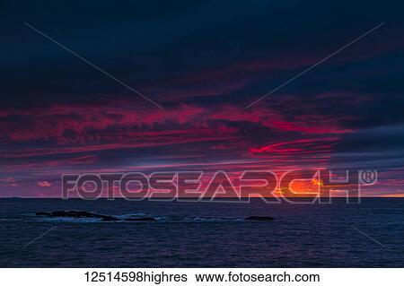 Stock Photograph - Clouds glowing a bright pink on the horizon over water; Bonavista, Newfoundland, Canada. Fotosearch