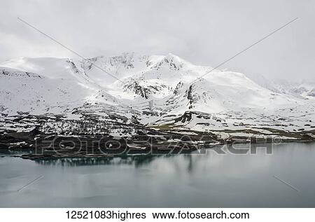 Stock Photograph - Col du Mont Cenis, Lake du Mont Cenis with snowy peak in background; Savoie, France. Fotosearch