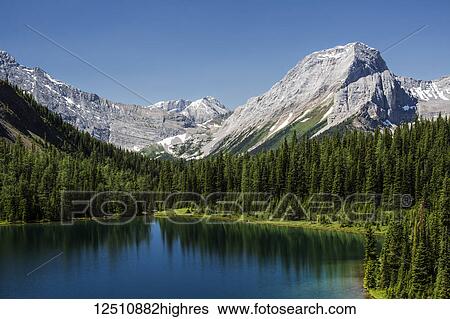 Stock Photograph - Colourful alpine lake surrounded by mountains and blue sky, Spray Lake Provincial Park; Kananaskis Country, Alberta, Canada. Fotosearch