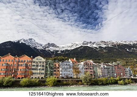 Colourful buildings along river bank with snow-covered mountain peaks, dramatic clouds and blue sky overhead; Innsbruck, Tyrol, Austria View Large Photo Image Stock Photograph - Colourful buildings along river bank with snow-covered mountain peaks, dramatic clouds and blue sky overhead; Innsbruck, Tyrol, Austria. Fotosearch