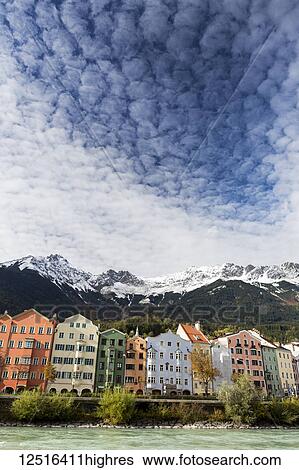 Colourful buildings along river bank with snow-covered mountain peaks, dramatic clouds and blue sky overhead; Innsbruck, Tyrol, Austria View Large Photo Image Stock Photograph - Colourful buildings along river bank with snow-covered mountain peaks, dramatic clouds and blue sky overhead; Innsbruck, Tyrol, Austria. Fotosearch
