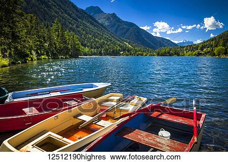 Stock Photograph - Colourful row boats with Champex Lake surrounded by mountains under blue sky, Alps; Champex, Switzerland. Fotosearch