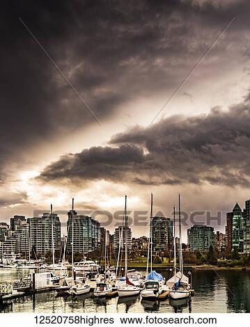 Stock Photograph - Condominium buildings and sailboats moored in the harbour under dark clouds; Vancouver, British Columbia, Canada. Fotosearch