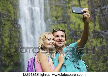 Couple Having Fun Together Outdoors. Taking Self Portrait With Camera Phone After Hiking To Incredible Waterfall In Hawaii. View Large Photo Image Stock Photograph - Couple Having Fun Together Outdoors. Taking Self Portrait With Camera Phone After Hiking To Incredible Waterfall In Hawaii.. Fotosearch