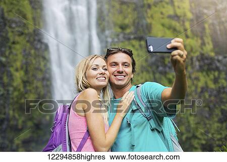 Couple Having Fun Together Outdoors. Taking Self Portrait With Camera Phone After Hiking To Incredible Waterfall In Hawaii. View Large Photo Image Stock Photograph - Couple Having Fun Together Outdoors. Taking Self Portrait With Camera Phone After Hiking To Incredible Waterfall In Hawaii.. Fotosearch