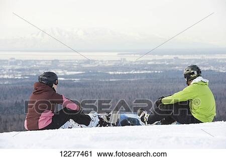Stock Image - Couple strap on their snowboards at the top of Hilltop Ski Area in Anchorage, Alaska. Fotosearch