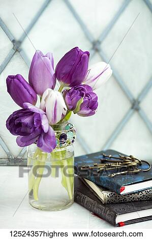 Stock Photograph - Cut tulips in a decorative glass jar with a pile of books and vintage keys. Fotosearch