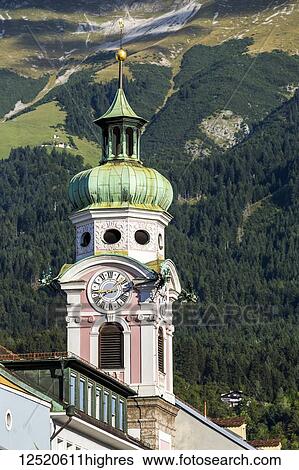Stock Photograph - Decorative church clock tower against a treed covered mountain slope background; Innsbruck, Tyrol, Austria. Fotosearch