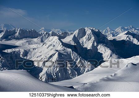 Stock Photograph - Dramatic landscape of the rugged, snow covered mountain ranges with shadows and blue sky; Haines, Alaska, United States of America. Fotosearch