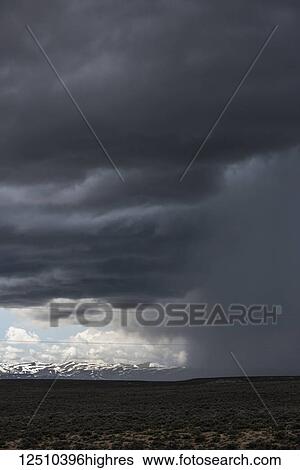Dramatic storm cloud gathered over an open field with a snow capped mountain range in the distance; Idaho, United States of America View Large Photo Image Stock Photograph - Dramatic storm cloud gathered over an open field with a snow capped mountain range in the distance; Idaho, United States of America. Fotosearch