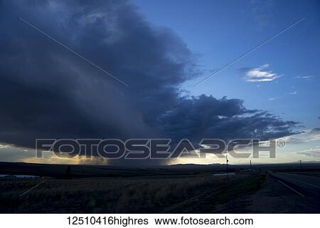 Dramatic storm clouds and falling rain on the horizon glowing with sunlight at sunset; Idaho, United States of America View Large Photo Image Stock Photograph - Dramatic storm clouds and falling rain on the horizon glowing with sunlight at sunset; Idaho, United States of America. Fotosearch