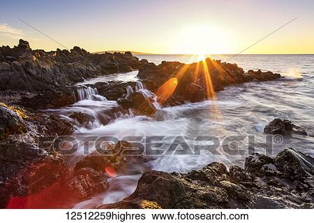 Stock Photograph - Dramatic sunset over the ocean with waterfalls along the rugged coastline; Wailea, Maui, Hawaii, United States of America. Fotosearch