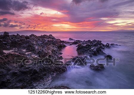 Stock Photograph - Dramatic sunset over the ocean with waterfalls along the rugged coastline; Wailea, Maui, Hawaii, United States of America. Fotosearch
