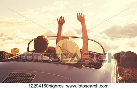 Stock Photograph - Driving Into The Sunset. Happy Young Couple Enjoying The Sunset In Classic Vintage Sports Car. Fotosearch