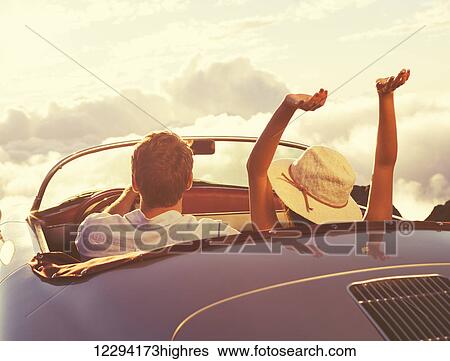 Stock Photograph - Driving Into The Sunset. Happy Young Couple Enjoying The Sunset In Classic Vintage Sports Car.. Fotosearch