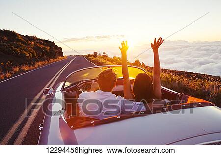 Stock Photograph - Driving Into The Sunset. Romantic Young Couple Enjoying Sunset Drive In Classic Vintage Sports Car. Fotosearch