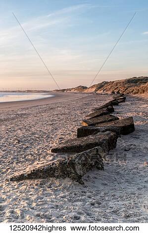 Stock Photograph - Early morning view of Amble beach showing a line of WWII concrete defences buried in the sand; Amble by the Sea, Northumberland, England. Fotosearch
