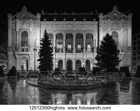Stock Photograph - Exterior of a building illuminated at nighttime by light, a frozen pool and fountain in the foreground; Budapest, Budapest, Hungary. Fotosearch
