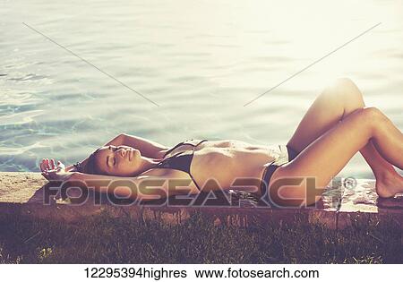 Stock Photograph - Fashion Lifestyle, Beautiful Woman In Swimwear Relaxing By The Pool At Sunset. Fotosearch