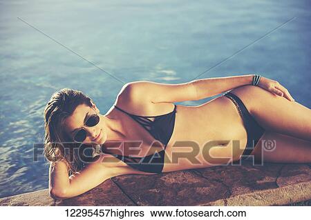 Stock Photograph - Fashion Lifestyle, Beautiful Woman In Swimwear Relaxing By The Pool At Sunset. Fotosearch