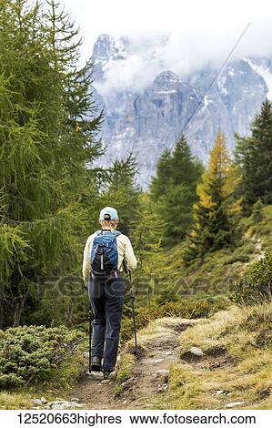 Stock Photograph - Female hiker along alpine trail with cloud covered mountains in the background; Sesto, Bolzano, Italy. Fotosearch