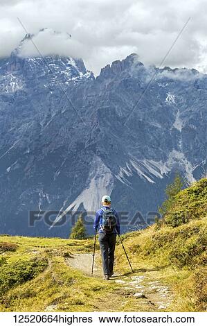 Stock Photograph - Female hiker along alpine trail with cloud covered mountains in the background; Sesto, Bolzano, Italy. Fotosearch