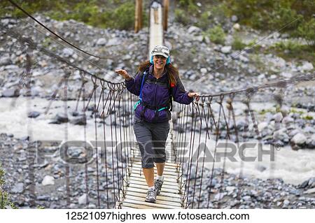 Stock Photograph - Female hiker crosses a wooden foot bridge on her way to Gulkana Glacier; Alaska, United States of America. Fotosearch
