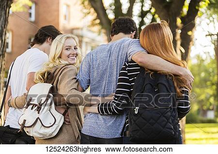 Stock Photograph - Four friends walking and talking in an embrace on the university campus with a female looking back at the camera; Edmonton, Alberta, Canada. Fotosearch