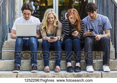 Four students sitting in a row on a step using their technology on the university campus; Edmonton, Alberta, Canada View Large Photo Image Stock Photograph - Four students sitting in a row on a step using their technology on the university campus; Edmonton, Alberta, Canada. Fotosearch