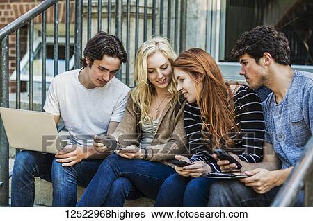 Four students sitting in a row on a step using their technology on the university campus; Edmonton, Alberta, Canada View Large Photo Image Stock Photograph - Four students sitting in a row on a step using their technology on the university campus; Edmonton, Alberta, Canada. Fotosearch