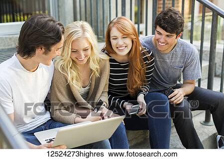 Four students sitting in a row on a step using their technology on the university campus and laughing together; Edmonton, Alberta, Canada View Large Photo Image Stock Photograph - Four students sitting in a row on a step using their technology on the university campus and laughing together; Edmonton, Alberta, Canada. Fotosearch