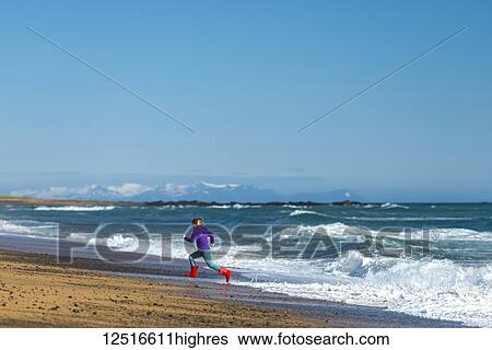 Stock Photograph - Girl running from waves on Langaholt beach; Langaholt, Iceland. Fotosearch
