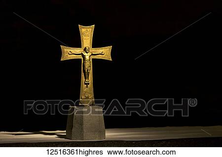Stock Photograph - Gold crucifix dramatically illuminated with black background; Florence, Tuscany, Italy. Fotosearch