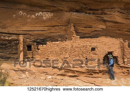 Stock Photograph - Hiker looking at Reverse Handprints, Ancestral Pueblo, up to 1, 000 years old, Bears Ears National Monument; Utah, United States of America. Fotosearch