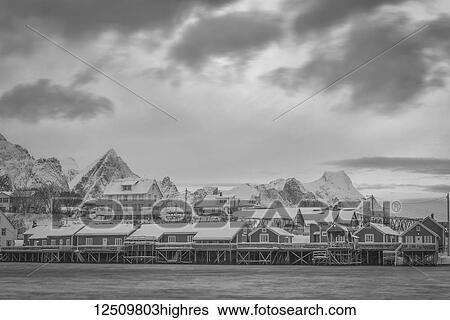Stock Photograph - Houses elevated on stilts along the water's edge with rugged mountains in the background and cloud; Svolvar, Lofoten Islands, Norland, Norway. Fotosearch