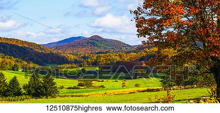 Stock Photograph - Landscape of forests on the hills with autumn coloured foliage and lush green fields in the foreground; Iron Hill, Quebec, Canada. Fotosearch