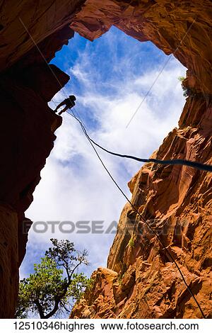 Stock Photograph - Looking upwards to the silhouette of an adventurer rappelling down a canyon in the desert; Hanksville, Utah, United States of America. Fotosearch