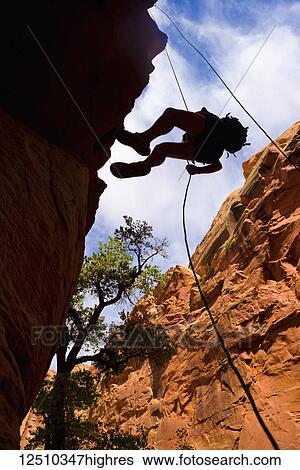 Stock Photograph - Looking upwards to the silhouette of an adventurer rappelling down a canyon in the desert; Hanksville, Utah, United States of America. Fotosearch