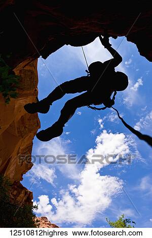 Stock Photograph - Looking upwards to the silhouette of an adventurer rappelling down a canyon in the desert; Hanksville, Utah, United States of America. Fotosearch