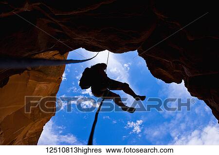 Looking upwards to the silhouette of an adventurer rappelling down a canyon in the desert; Hanksville, Utah, United States of America View Large Photo Image Stock Photograph - Looking upwards to the silhouette of an adventurer rappelling down a canyon in the desert; Hanksville, Utah, United States of America. Fotosearch