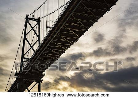 Low angle view of a bridge at sunset with an airplane flying in the distance; Vancouver, British Columbia, Canada View Large Photo Image Stock Photograph - Low angle view of a bridge at sunset with an airplane flying in the distance; Vancouver, British Columbia, Canada. Fotosearch