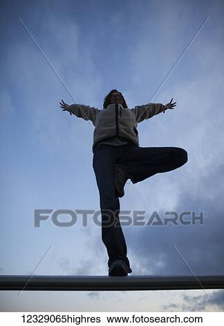 Stock Photograph - Low angle view of a woman doing a yoga pose on a beam with blue sky and cloud; Alaska, United States of America. Fotosearch